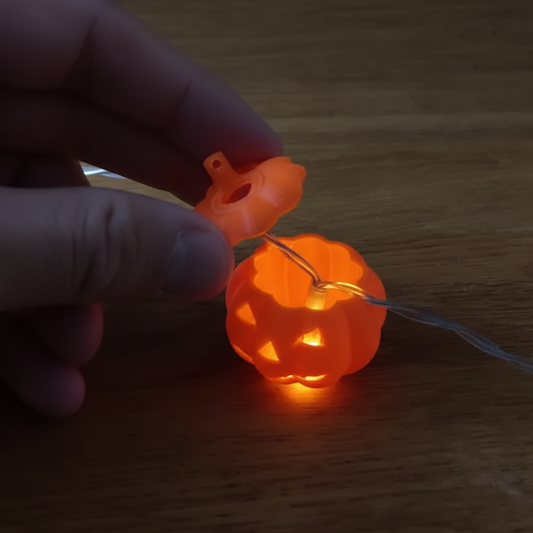 Hand holding a small glowing orange pumpkin-shaped light on a wooden surface
